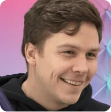 Smiling young man with short brown hair wearing a black hoodie against a colorful gradient background.
